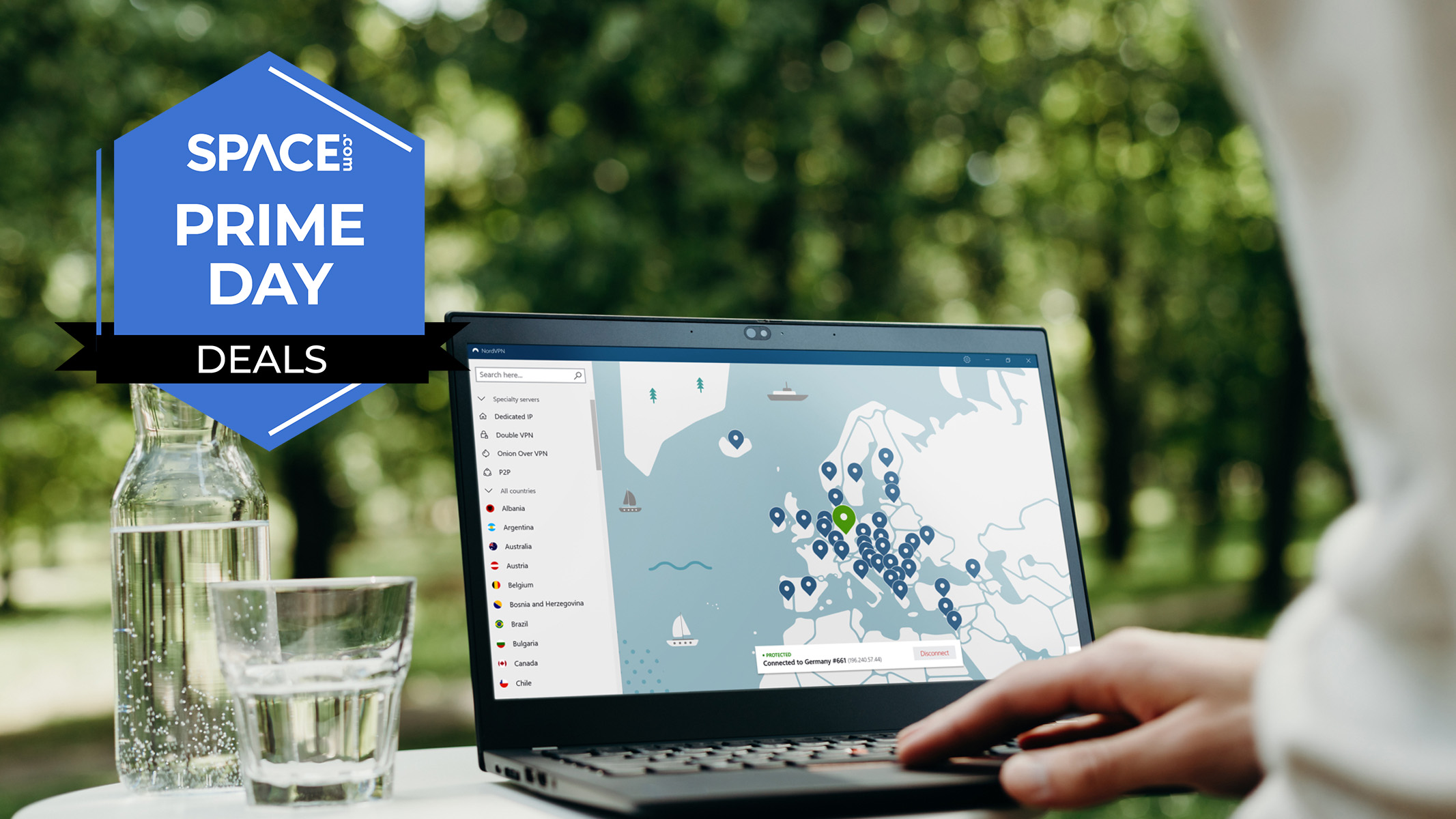 NordVPN running on a laptop, set on table outside next to a glass and bottle of water. A person is pressing the keys. 